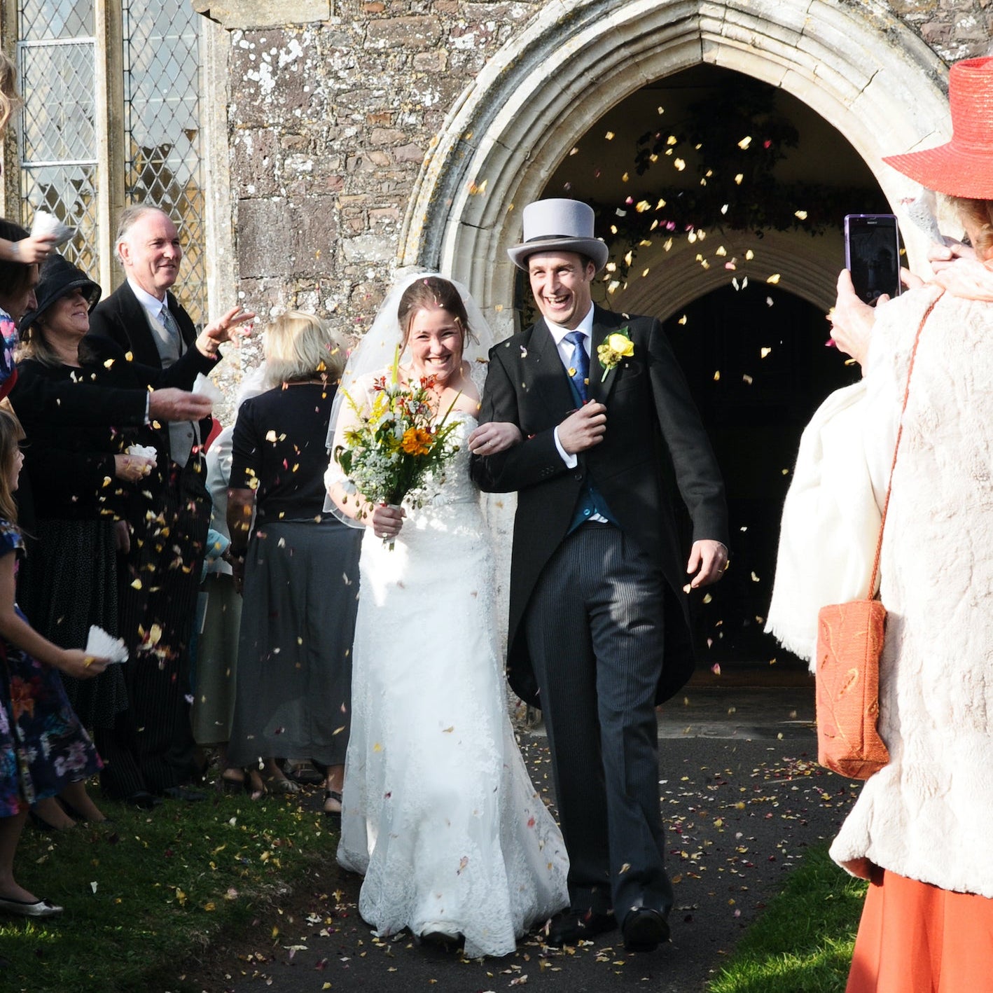 Wedding couple exiting church with guests throwing confetti.